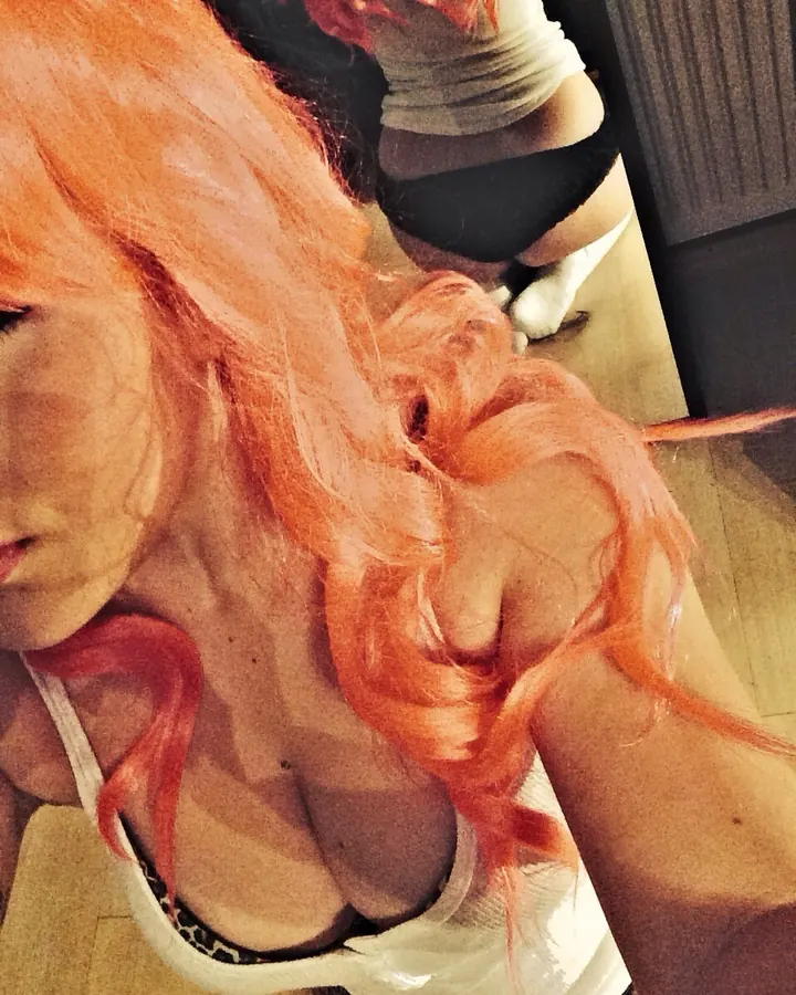 Femme européenne aux cheveux roux portant une lingerie rouge, allongée sur un lit.