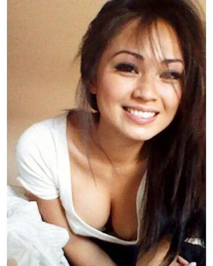 Femme asiatique aux cheveux noirs, portant un haut blanc, posant devant un mur extérieur, main dans les cheveux