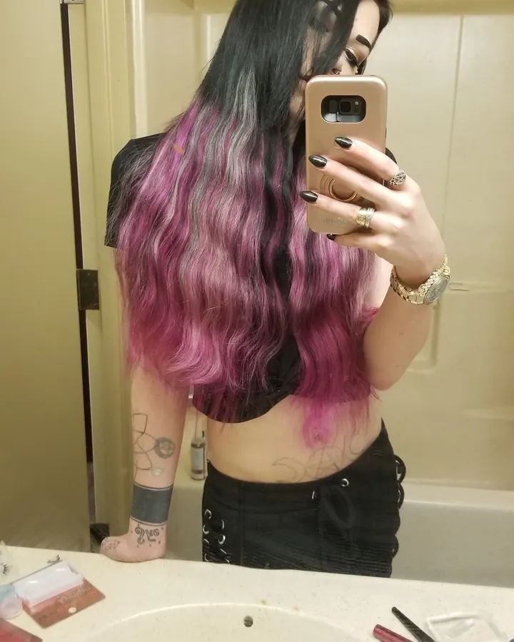Femme aux cheveux roux en maillot de bain noir, debout sur une plage blanche, une main dans les cheveux