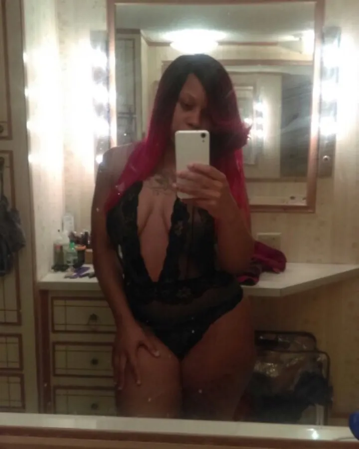 Femme aux cheveux roux en lingerie noire, prenant un selfie devant un miroir éclairé